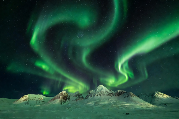 Intense ribbons of green aurora borealis curling across the Arctic sky above snowy mountain peaks