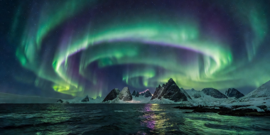 Northern lights arching over coastal waters and peaks near Tromsø and Kvaløya